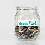 oins in a clear glass jar with house fund sign.